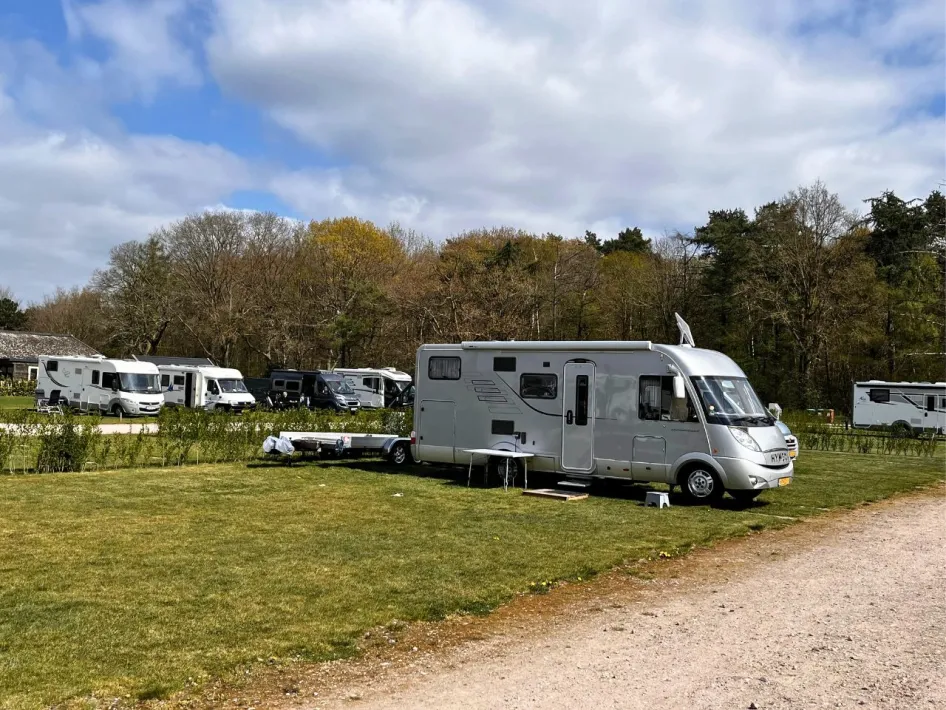 Several RVs are parked in spacious grassy areas near an RV park, overlooking a wooded area.