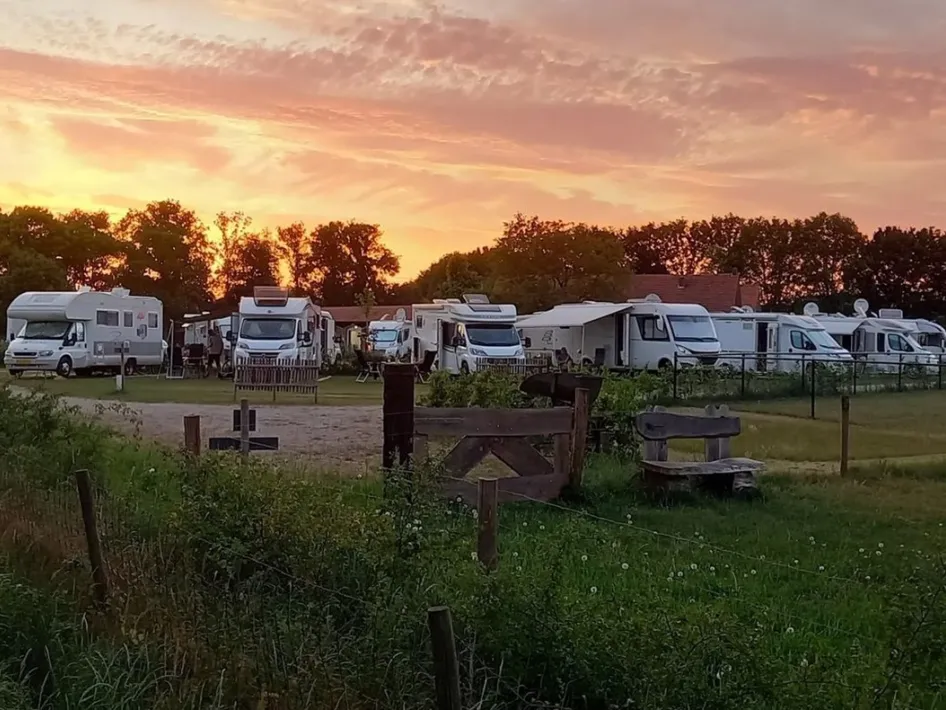 Wohnmobile stehen auf dem Wohnmobilstellplatz Houbenhof, während die Sonne untergeht und der Himmel warm orange leuchtet