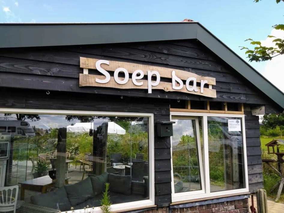 Gebouw van de soepbar bij Camperplaats Houbenhof met zitplekken binnen en uitzicht op de camperplaats