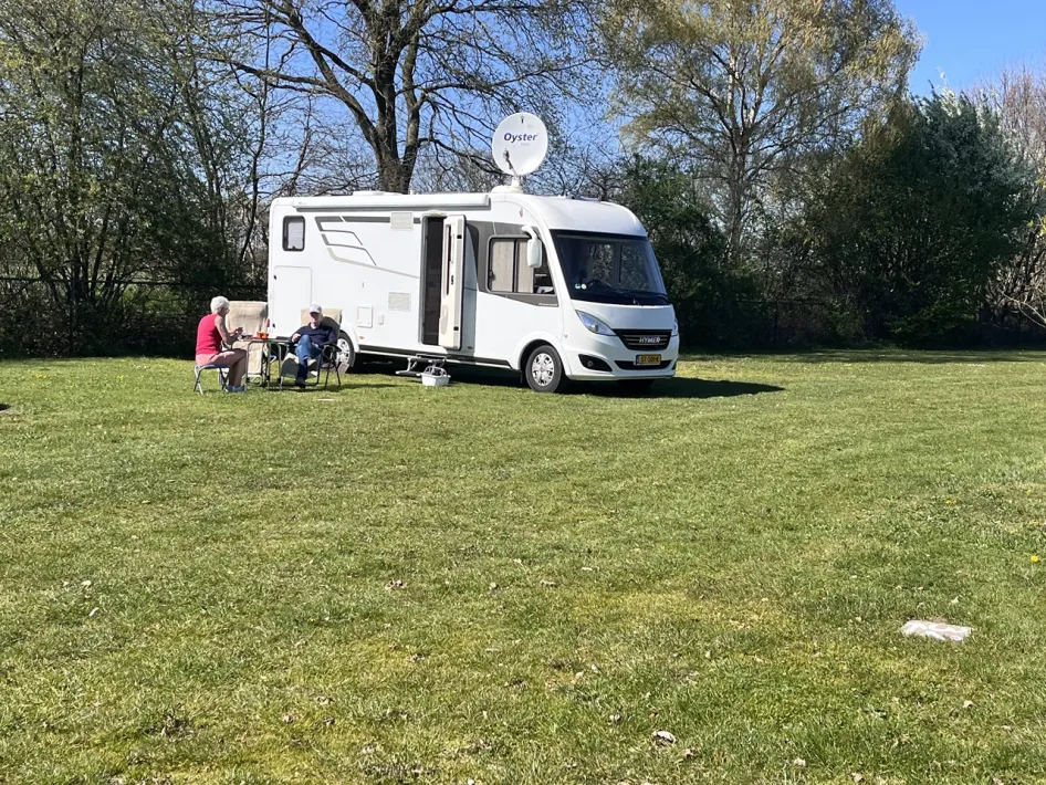 Stel zit ontspannen naast hun camper op het grasveld van de camperplaats.