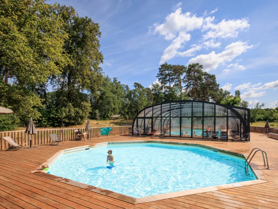 Outdoor pool with wooden deck and covered swimming area, surrounded by trees