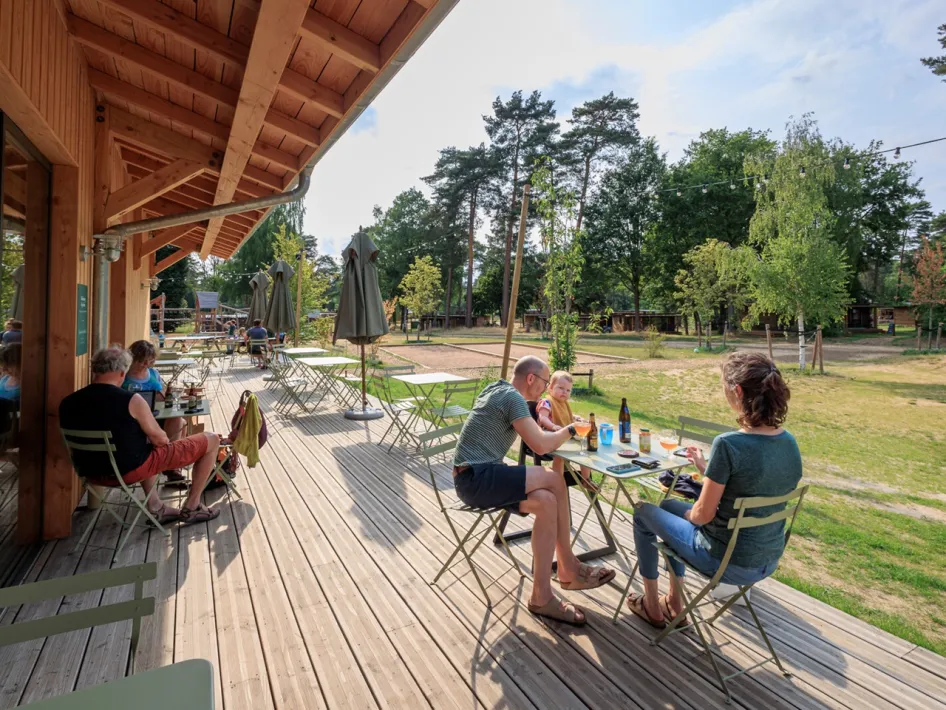 People eating and drinking on the terrace in front of the wooden reception building