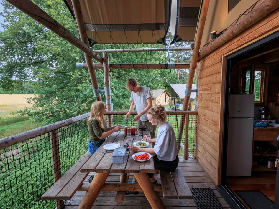 Three people dining on the veranda of a glamping tent with a view of the field