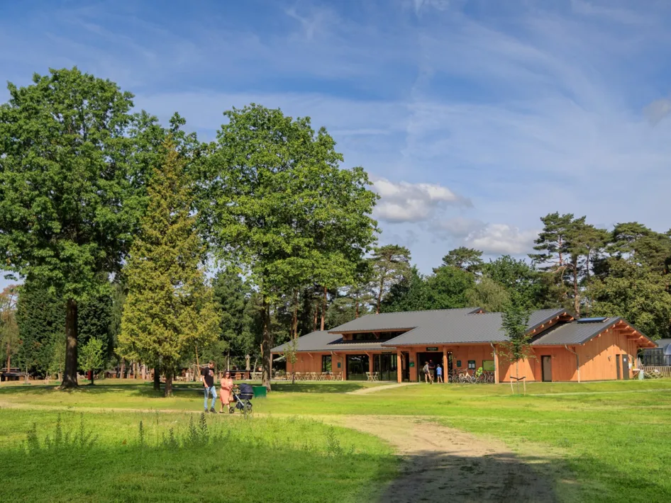 Wooden reception building with lawn and trees, people walking on the path