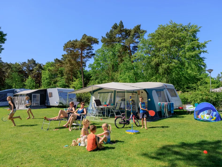 Kinderen spelen voor de tent terwijl de mama's heerlijk van de zon genieten