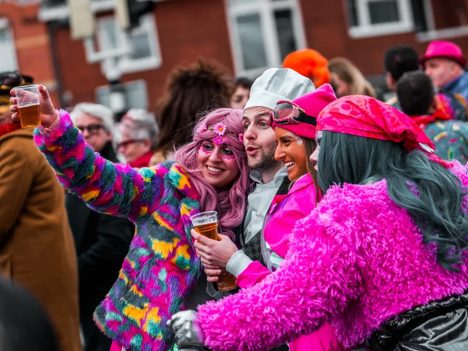 Dressed-up partygoers enjoy the atmosphere during the Carnival Procession Weert, laughing, toasting drinks and posing for a photo.