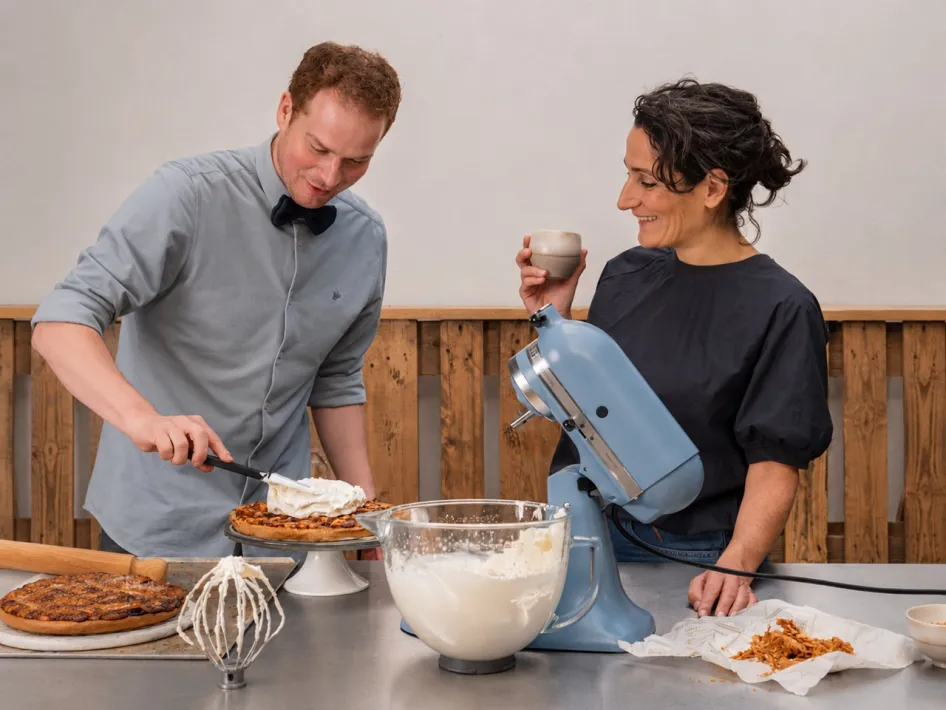 Cas Wolters brengt slagroom aan op een Limburgse vlaai terwijl Suzanne Heuts naast hem toekijkt.