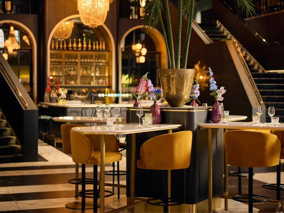 Interieur des Cerise Restaurant mit hohen Tischen, ockerfarbenen Stühlen, Blumen und warmer Beleuchtung.
