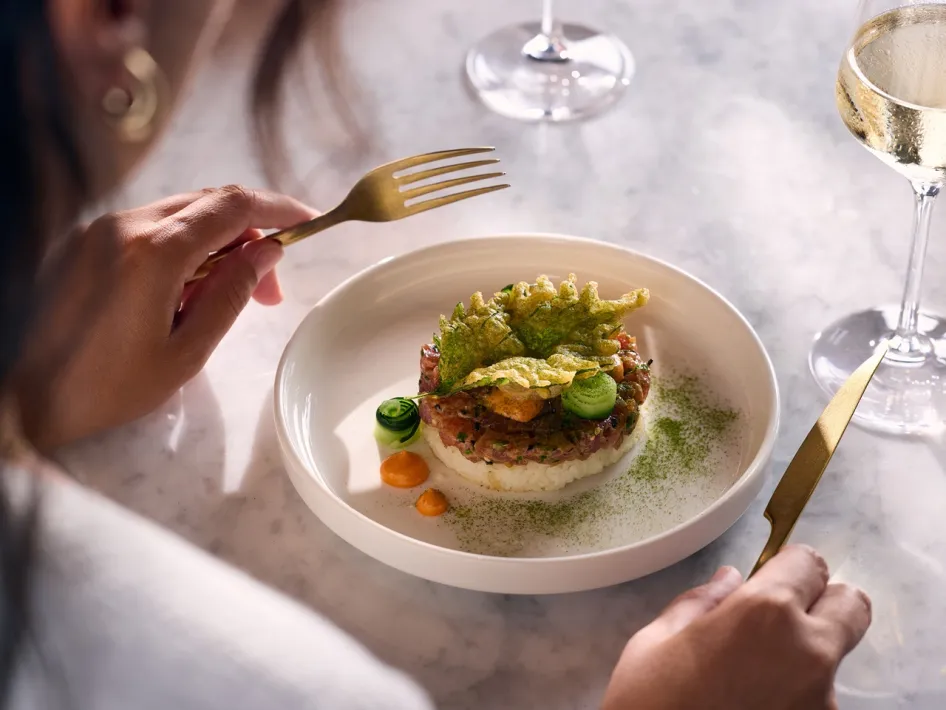 Guest at a table in Cerise Restaurant with a beautifully presented dish and a glass of white wine.