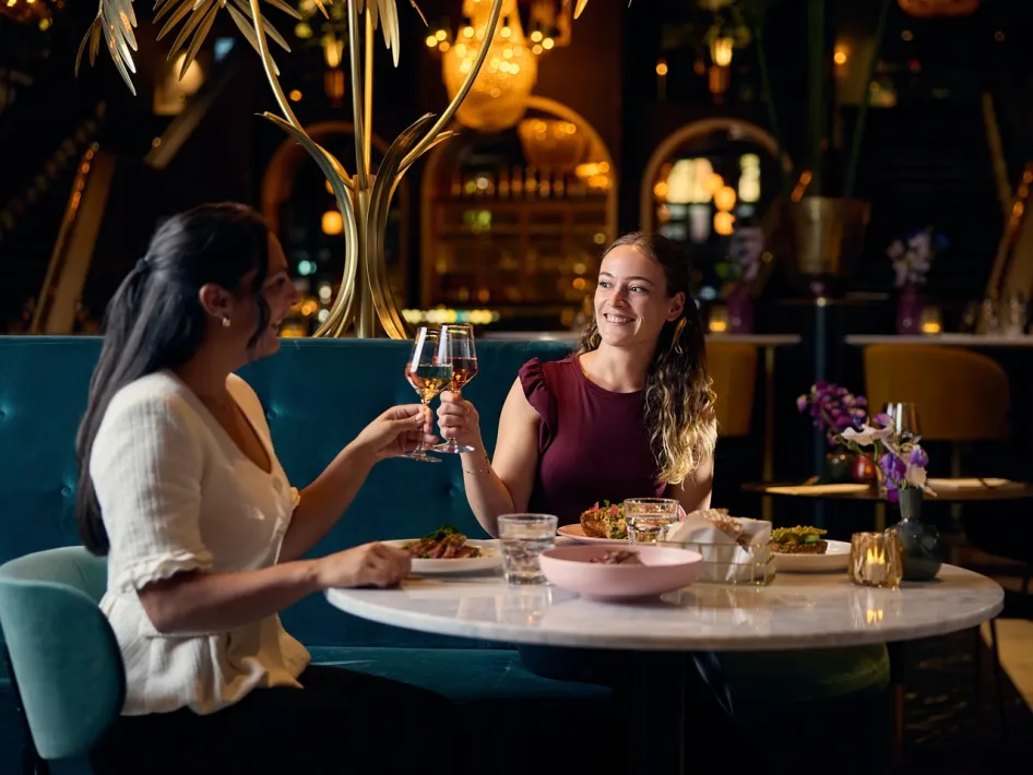 Twee vrouwen proosten tijdens een diner bij Cerise Restaurant, met gerechten en bloemen op tafel.