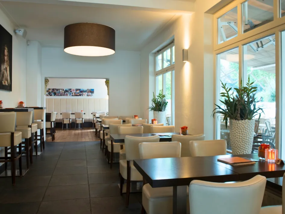Modern and attractive interior of Ice Cream Parlor Clevers Overloon with white chairs, dark tables and large plants.