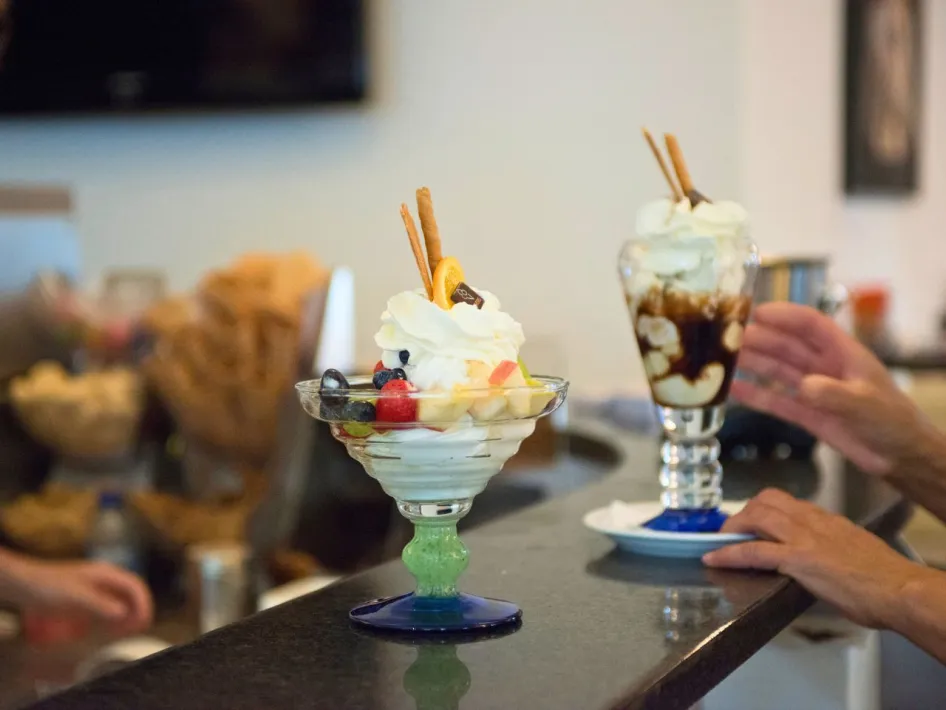 Two richly decorated ice cream sundaes on a bar, with whipped cream, fruit and cookies, served in an ice cream parlor.
