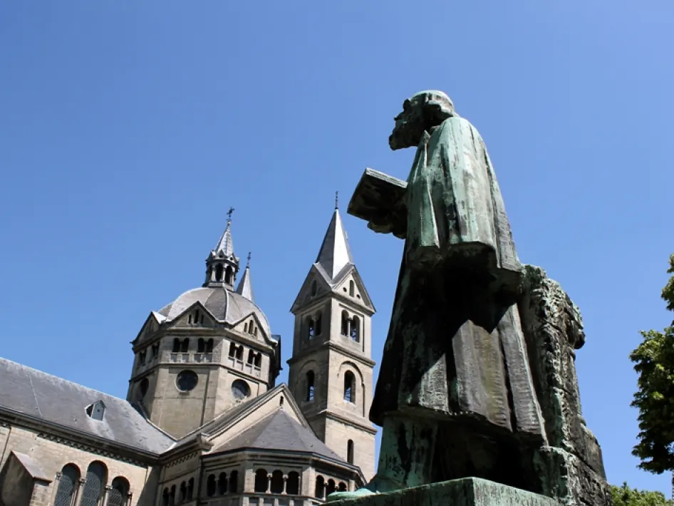 Standbeeld van Pierre Cuypers met op de achtergrond de karakteristieke torens van de Munsterkerk in Roermond, gezien vanaf het plein bij helderblauwe lucht.
