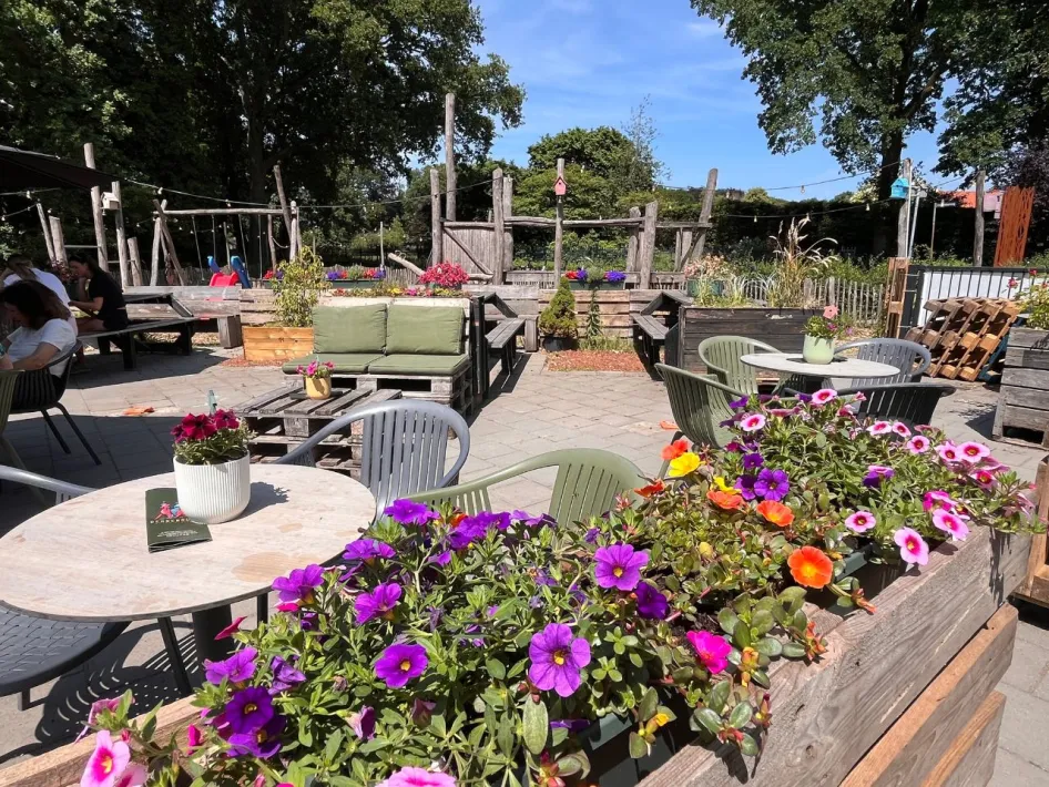 Zonnig terras met kleurrijke bloemen en speeltuin bij DENNENOORD Beers & Bites.