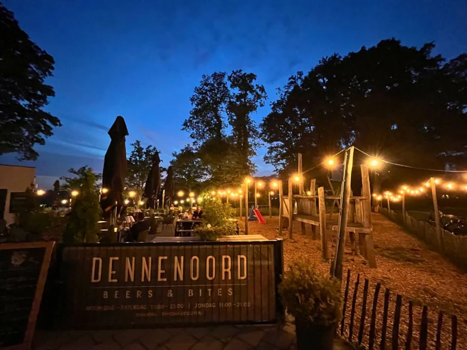 DENNENOORD Beers & Bites - Avondsfeer op het terras met sfeerverlichting en speeltuin op de achtergrond.