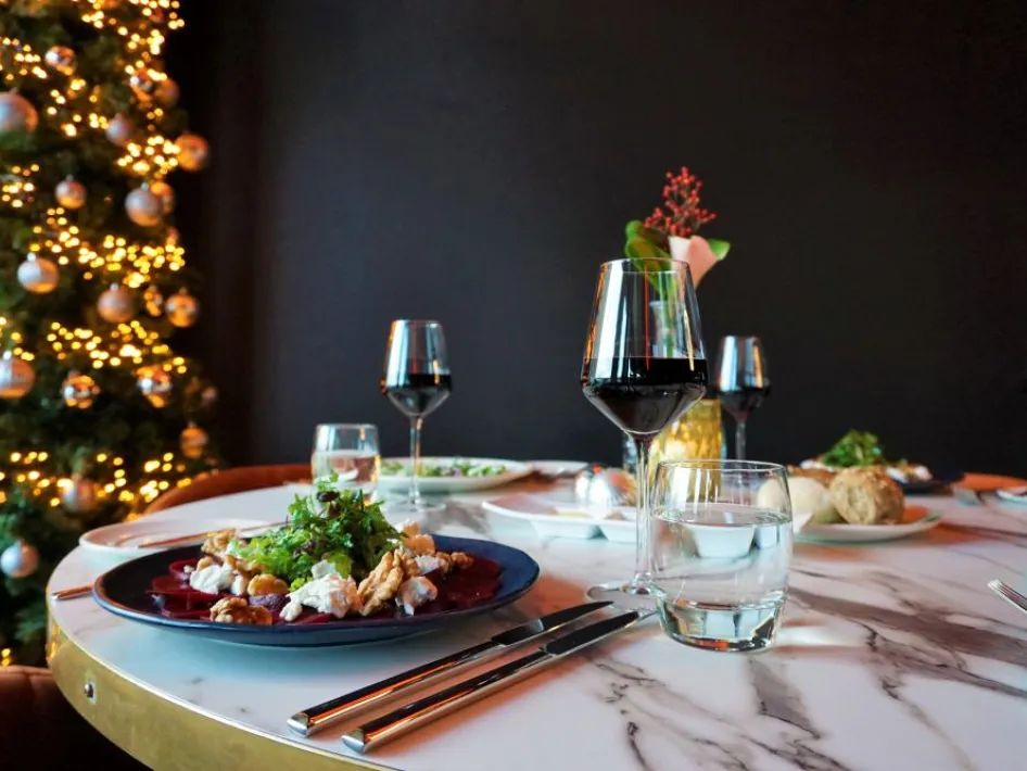 Gedekte tafel voor het Kerst Diner Dansant bij Parkhotel Horst, met feestelijke gerechten, rode wijn en een versierde kerstboom op de achtergrond.