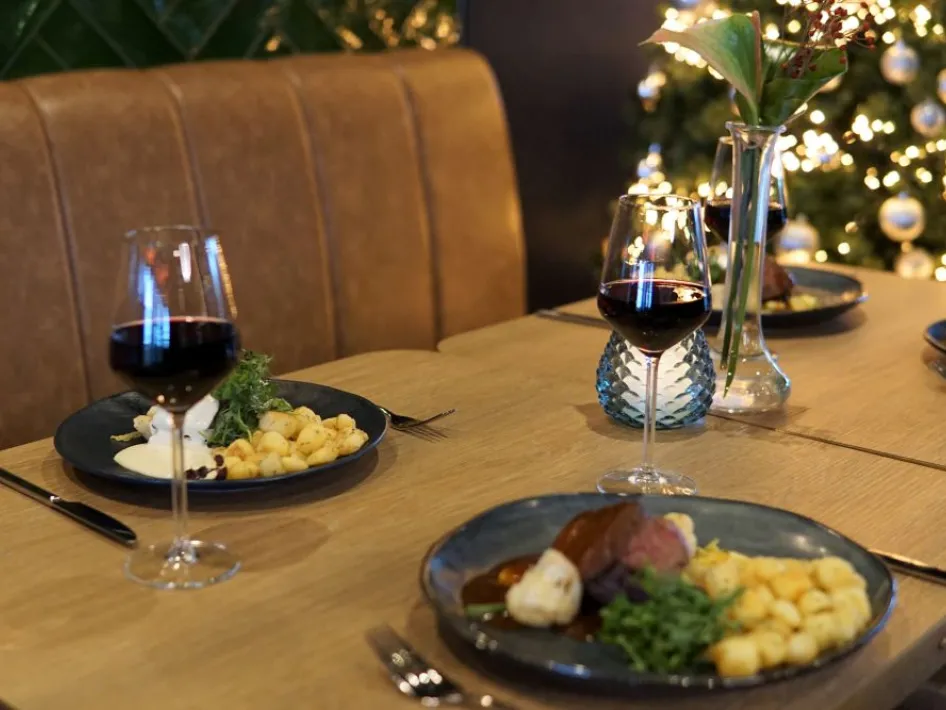 Diner tijdens het kerst familiebuffet bij Parkhotel Horst, met borden vol feestelijke gerechten, rode wijn en kerstboom op de achtergrond.