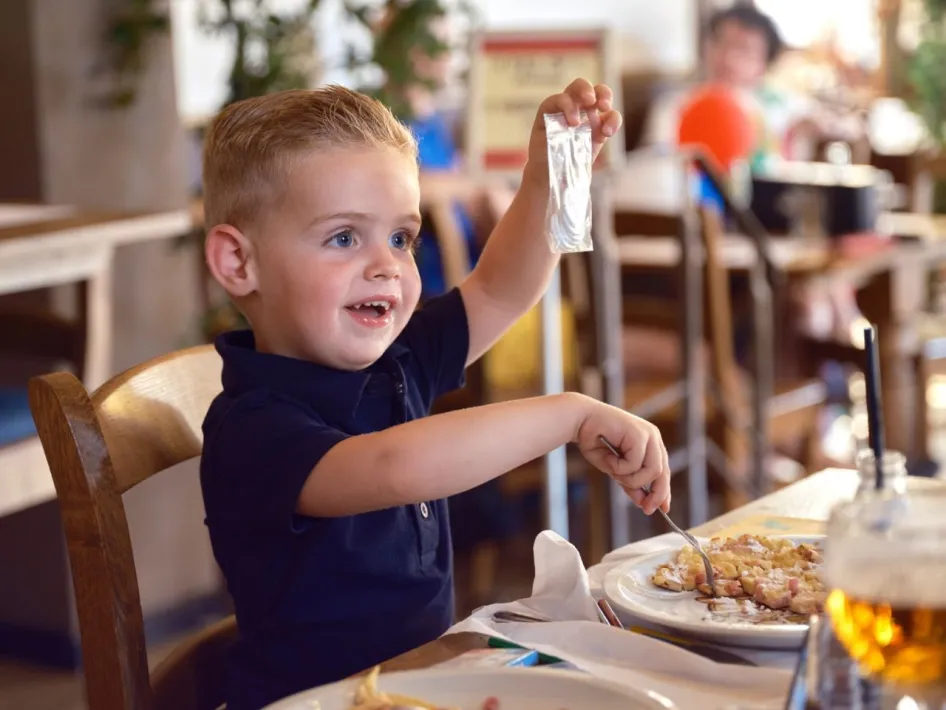 Fröhlicher Junge isst einen Pfannkuchen im De Pannekoekenbakker und hält stolz eine Smulmunt-Münze hoch.