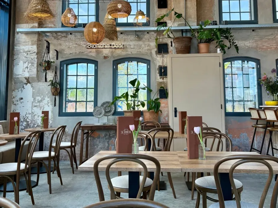 Stimmungsvolles Interieur von La Comida mit Holztischen, Rattan-Hängeleuchten und großen Fabrikfenstern in De Pannenfabriek in Echt.