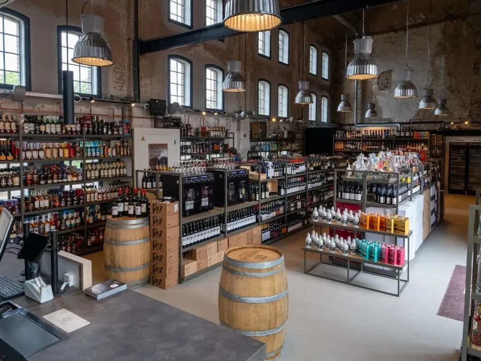 Innenansicht von Maxwijn mit Regalen voller Wein und anderer Getränke in einer historischen Fabrikhalle von De Pannenfabriek in Echt.