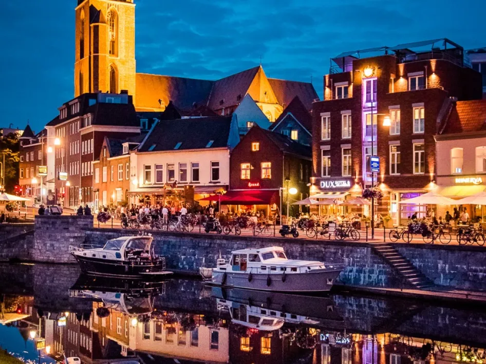 Avondsfeer aan de Roerkade in Roermond met verlichte cafés, mensen op terrassen en dobberende boten tijdens Dreijaovend Roermond.