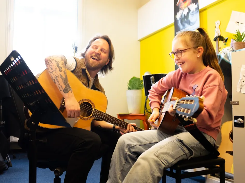 Gitarrenunterricht in der ECI Cultuurfabriek, bei dem Lehrkraft und Schüler gemeinsam musizieren.