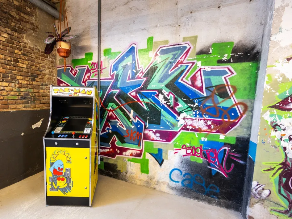 Yellow Pac-Man arcade machine at ECI Roermond, next to a colourful graffiti-covered wall in an industrial space.