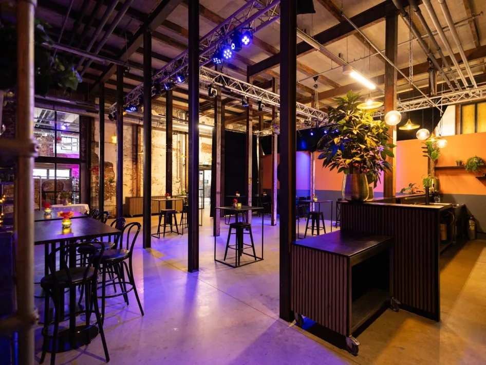 Industrial-style meeting space at ECI Roermond with high tables, black bar stools, plants and atmospheric purple lighting.