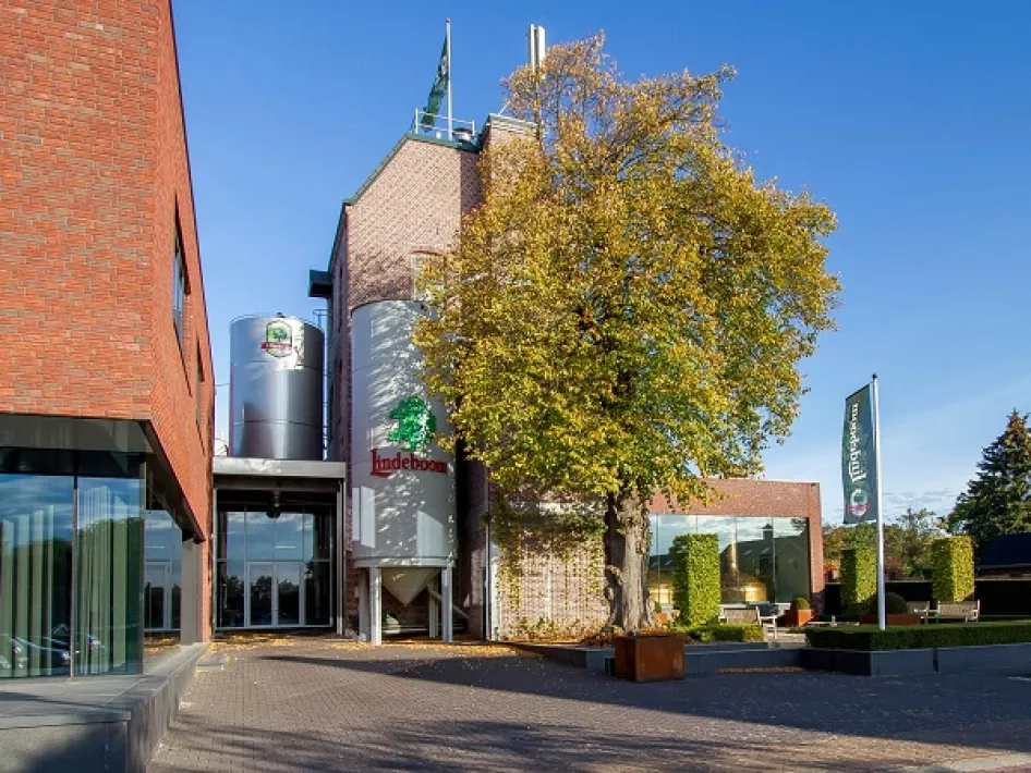 Exterieur van de brouwerij met silo’s en opvallend boom in herfstkleuren naast de hoofdingang.
