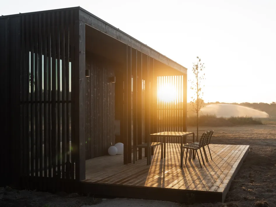 Donkerhouten lodge van Eco by Nature in Heythuysen met een ruim houten terras, zitje en uitzicht op de natuur bij zonsondergang.