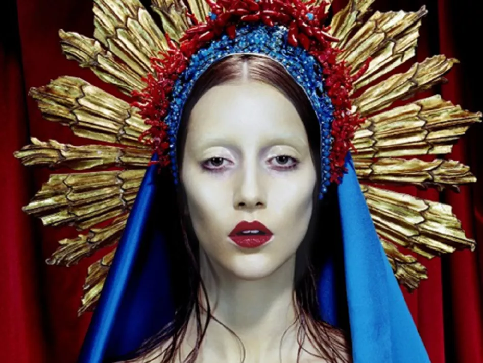 Kunstwerk uit de tentoonstelling Erotiek – Voorbij schoonheid en schaamte in het Limburgs Museum, met een vrouwelijk figuur in een koninklijk blauwe mantel en een gouden stralenkrans, tegen een rode achtergrond.