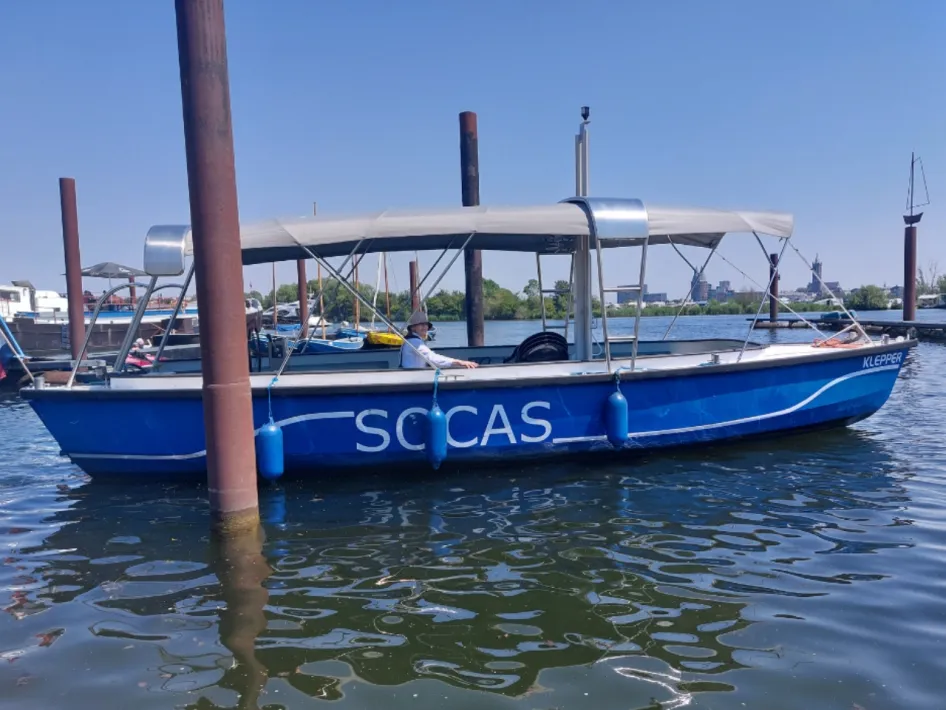 Blauwe rondvaartboot met de naam SOCAS aan de steiger, liggend op rustig water onder een heldere blauwe lucht.