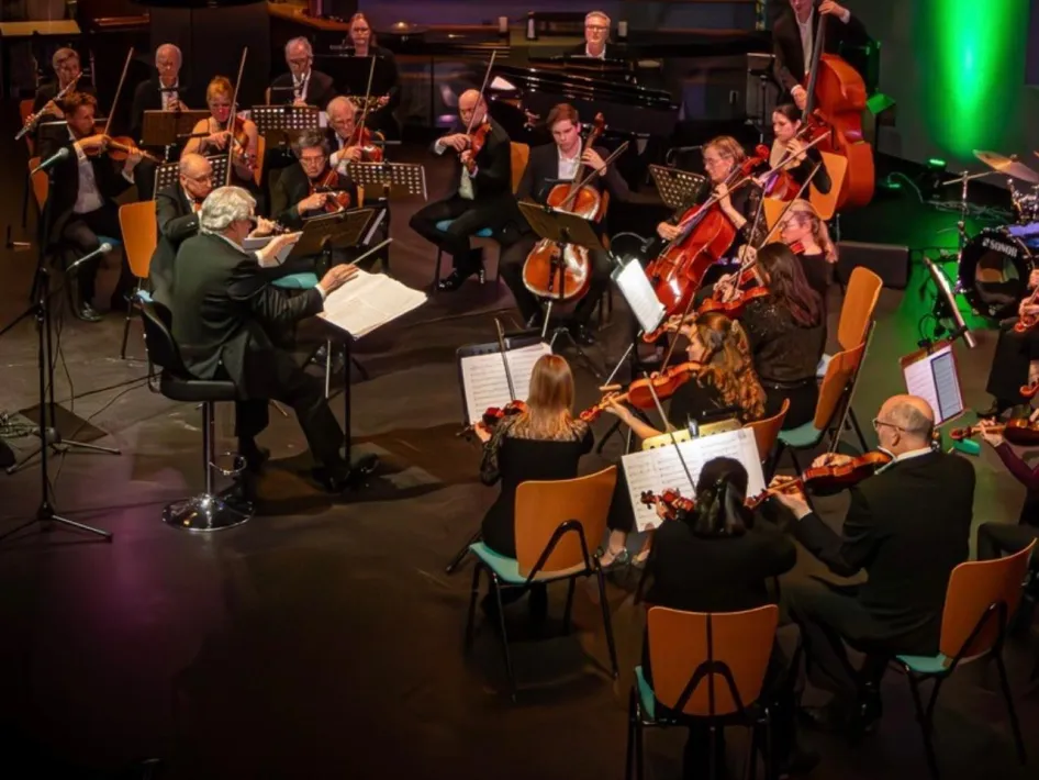 Het Vegas Orchestra onder leiding van de dirigent tijdens een concert met strijkers en vleugel op het podium.
