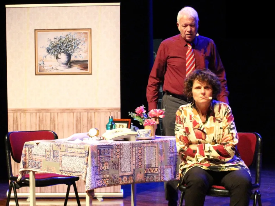 Theaterscène van De dementie van Jet & Harrie tijdens een bijeenkomst van Alzheimer Café Maasgouw, met twee acteurs die de impact van dementie uitbeelden in een huiskamersetting.