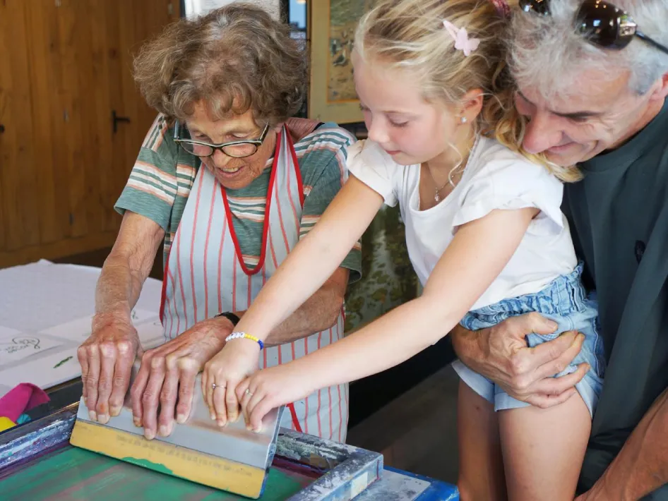 Kind en grootouders drukken samen een zeefdruk tijdens Drukkersdag bij Eynderhoof.