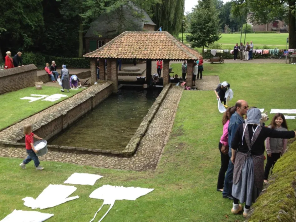 Historisch schouwspel bij de Sprunk in Baarlo, met wasgoed op het gras en bezoekers rond de historische waterbron.