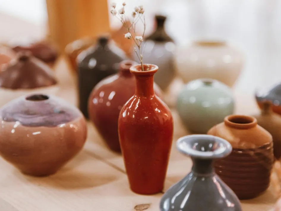 Keramieken vazen in verschillende vormen en aardetinten op een houten tafel, met een rood vaasje met een takje centraal in beeld