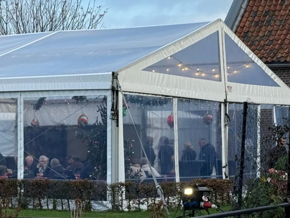Bezoekers zitten samen in een verlichte tent bij de kerststal van de Zusters Birgittinessen in Weert.