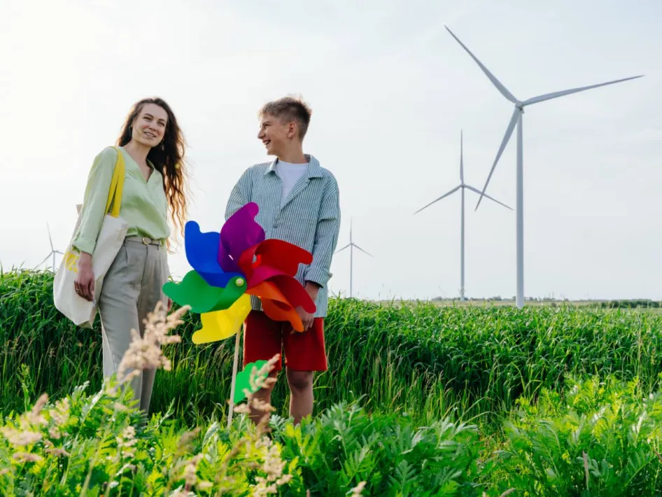 Twee bezoekers van Klimaatfestival STROOM staan in het groen bij windmolens en een kleurrijke windmolen.