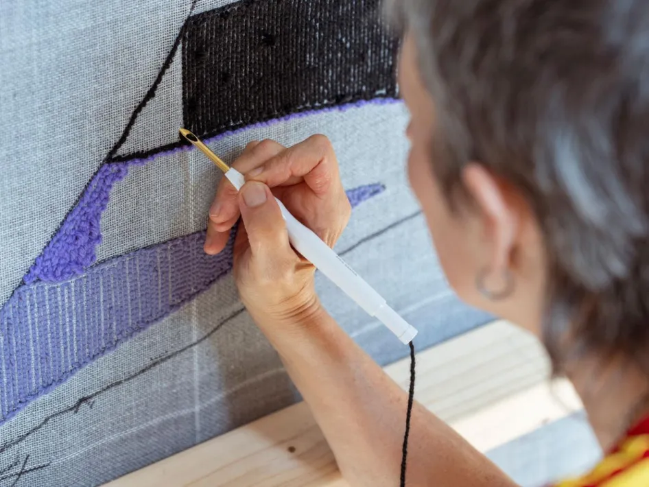 Close-up van hand die met punchnaald werkt aan detail van wandkleed