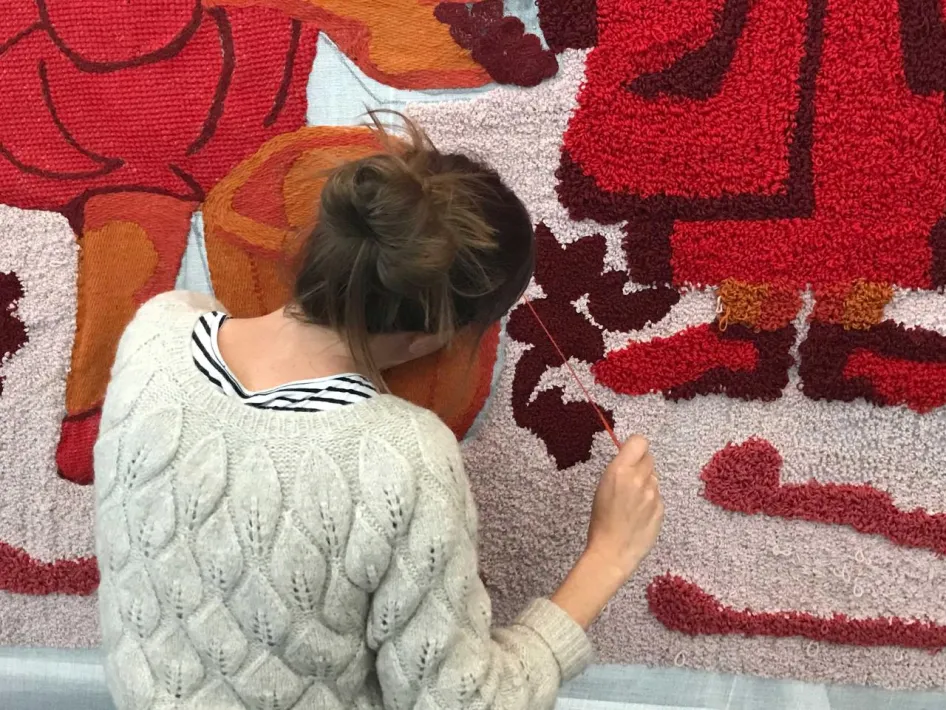 Deelnemer tuft met rode garens aan groot wandkleed in ontwikkeling