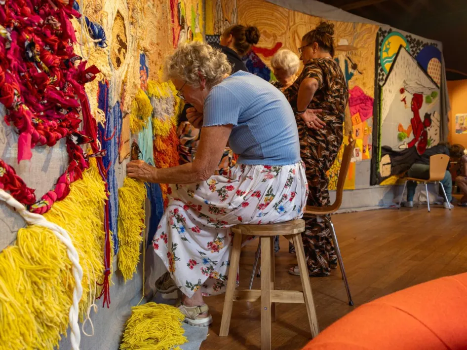 Vrouw werkt met kleurrijke stoffen aan gezamenlijk wandkleed in Museum van de Vrouw