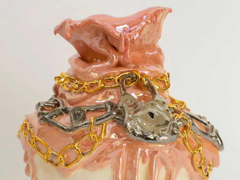 Glasiertes Keramikobjekt mit tropfenden rosafarbenen Formen, verziert mit gold- und silberfarbenen Ketten und einem Vorhängeschloss.
