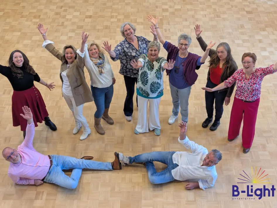 Alt-tekst: Gospelgroep B-Light treedt op tijdens het Peelpodium bij Buitencentrum De Pelen, waar de zangers enthousiast poseren voor een groepsfoto.