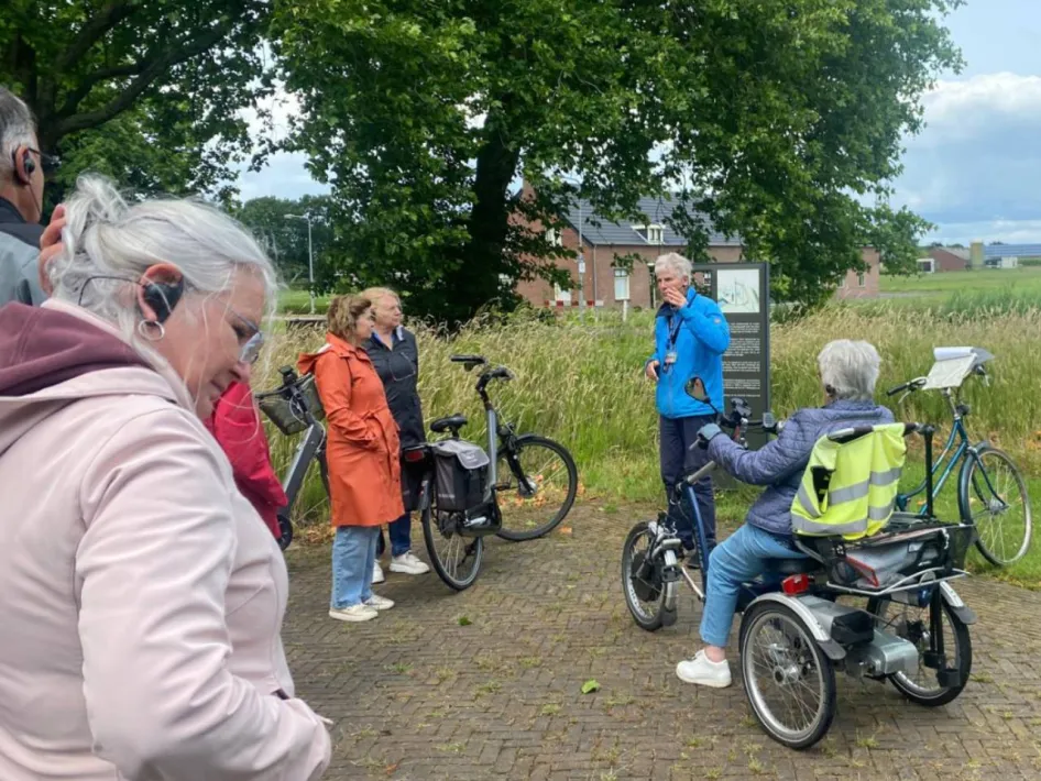 Deelnemers aan de Fietstocht Rondje Weert luisteren met hun fiets naar uitleg van de stadsgids bij een informatiebord in het groene buitengebied van Weert.