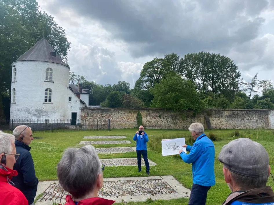 Stadsgids geeft uitleg aan deelnemers van de Fietstocht Rondje Weert bij een historische witte toren in het groen.