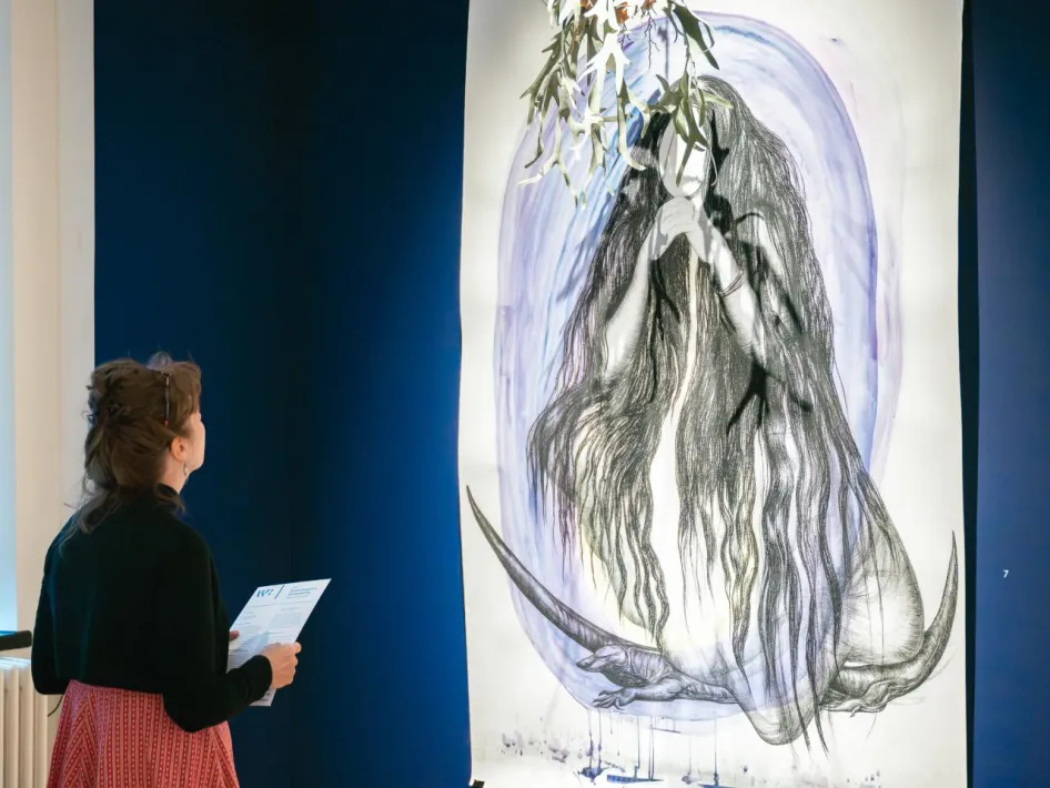 Bezoeker bekijkt een tekening van Danielle Lemaire tijdens de tentoonstelling die inspireert voor de Zomerse tekenworkshops.