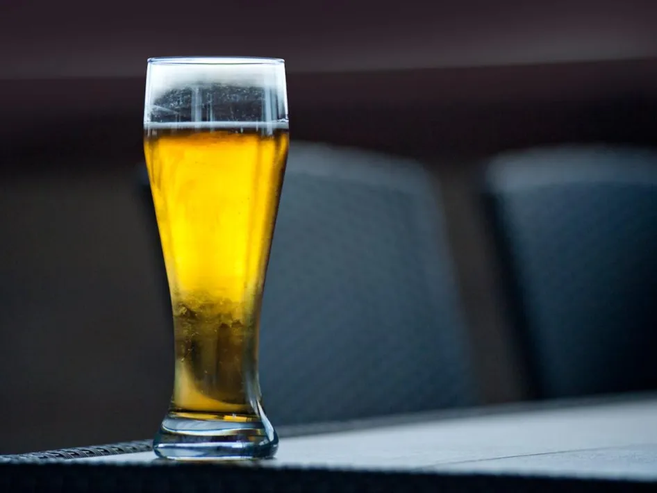 Glas goudkleurig bier met schuimkraag op tafel in een rustige barruimte.