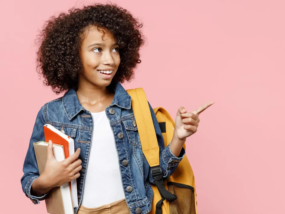 Leerling met rugzak en boeken wijst opzij met een glimlach, klaar voor school of examenperiode om examenstress tegen te gaan.