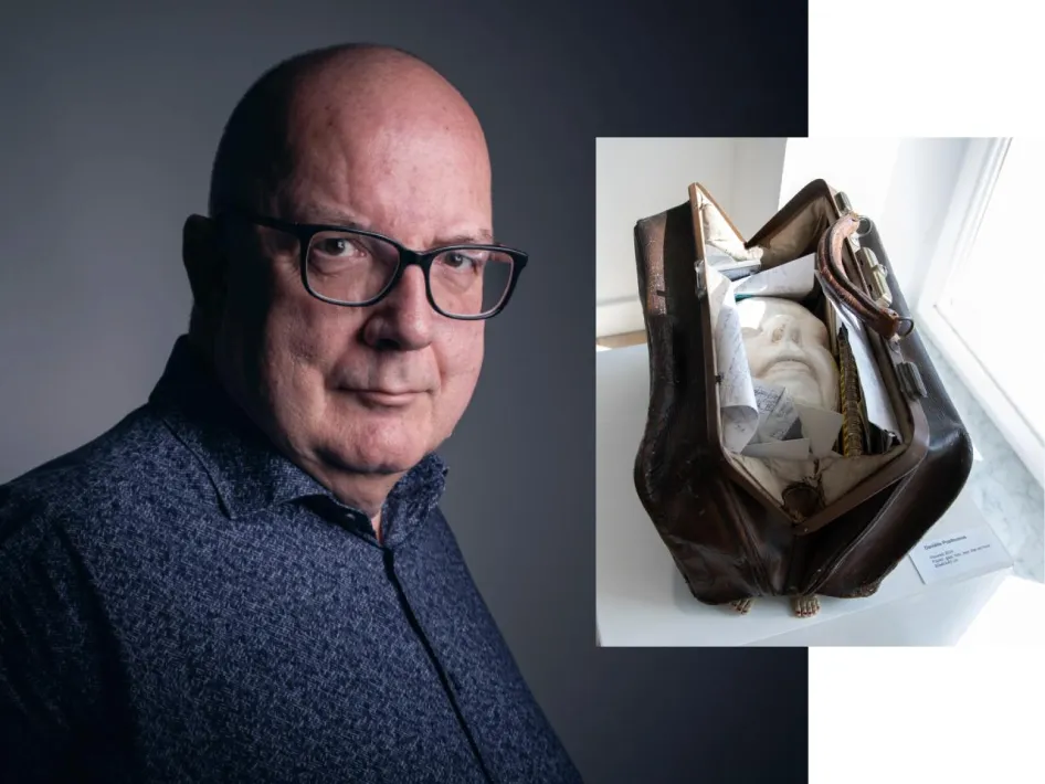 Portret van gespreksleider Ger Dierx naast een kunstwerk uit de tentoonstelling Opgebrand: een open leren tas met een gezichtsmasker en persoonlijke voorwerpen.